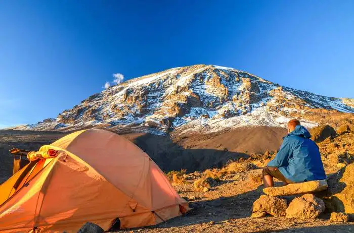 A climber on one of the Kilimanjaro travel routes, with tents in the background.
